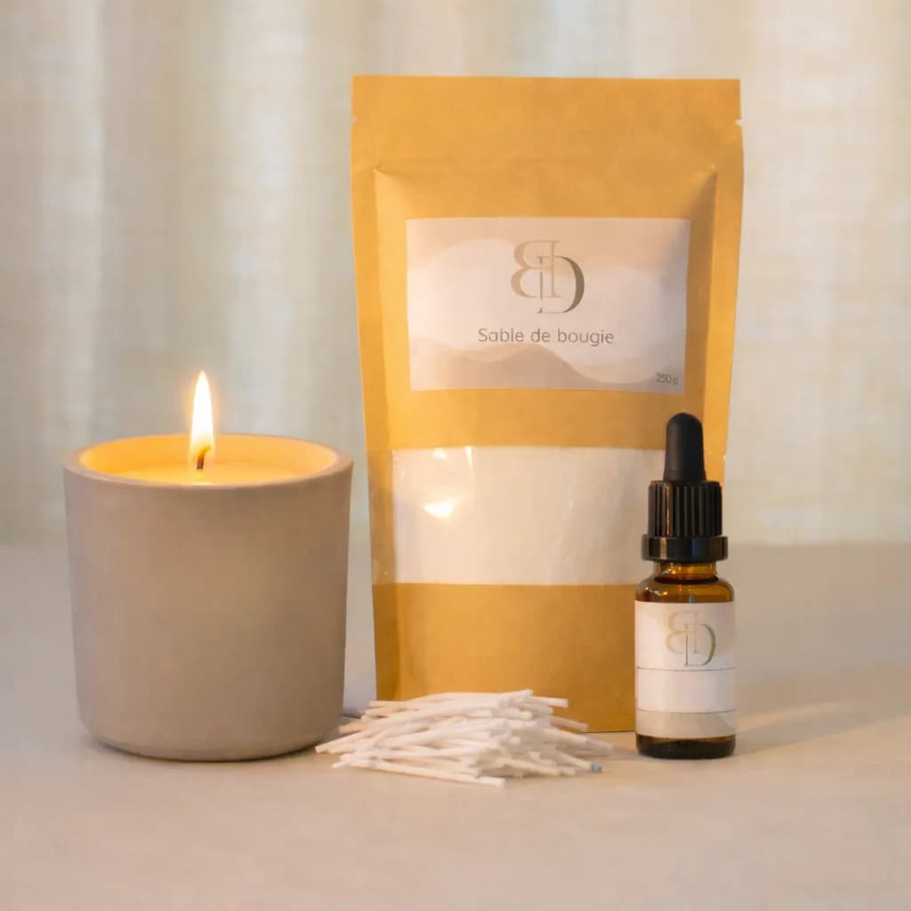 Bougie allumée à côté d'un sachet de sable, d'une fragrance et de mèches